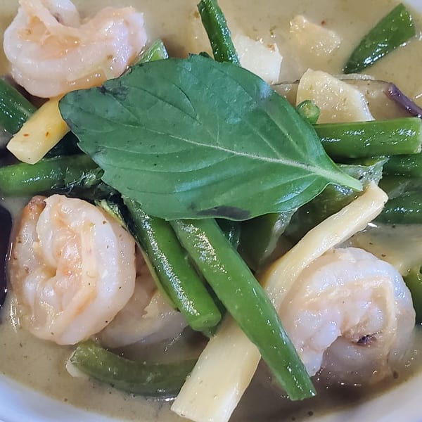 Close-up of Baan Thai green curry with shrimp, green beans, and bamboo shoots, garnished with basil.