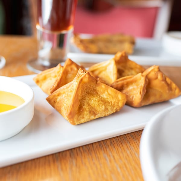 Crispy golden Baan Thai crab rangoons with a dipping sauce on a white plate.