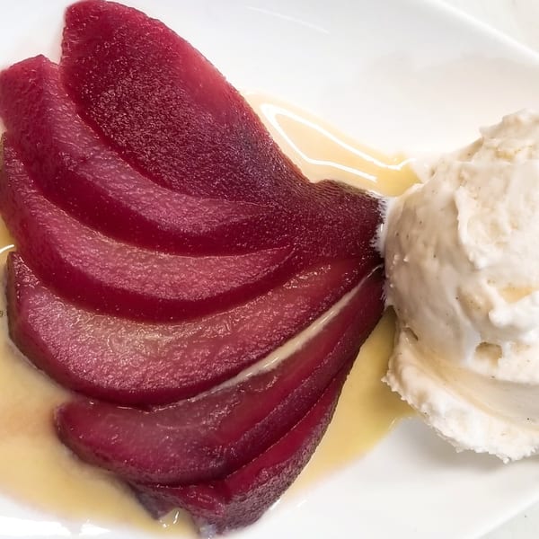 Sliced red pears in syrup with a scoop of vanilla ice cream on a white plate.