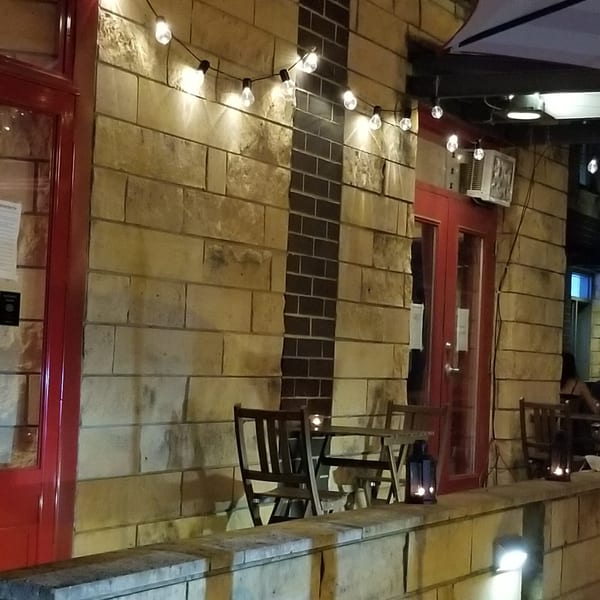 Exterior of Baan Thai restaurant at night, with string lights, red doors, and outdoor seating.
