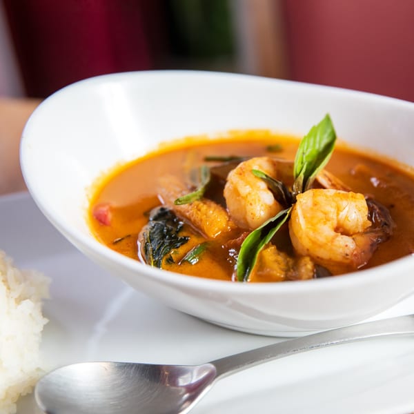 Baan Thai red curry with shrimp and basil, served with white rice and a spoon.