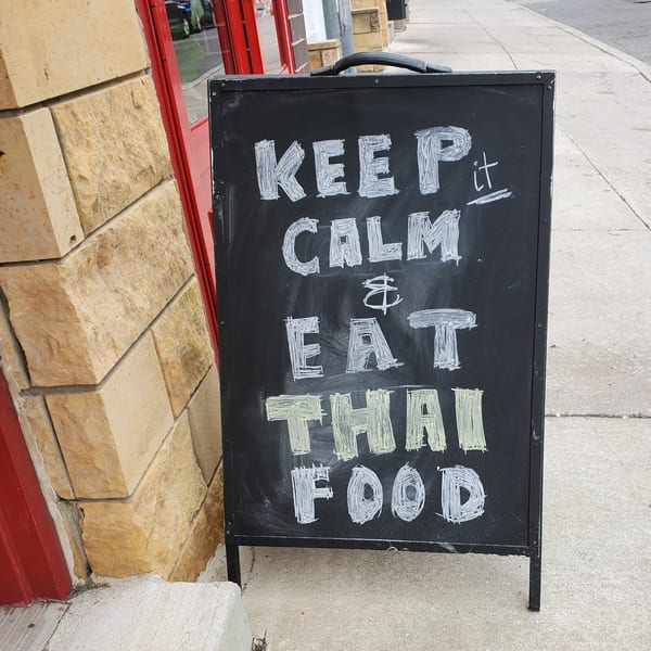 Chalkboard sign outside Baan Thai restaurant reads: "KEEP it CALM & EAT THAI FOOD".