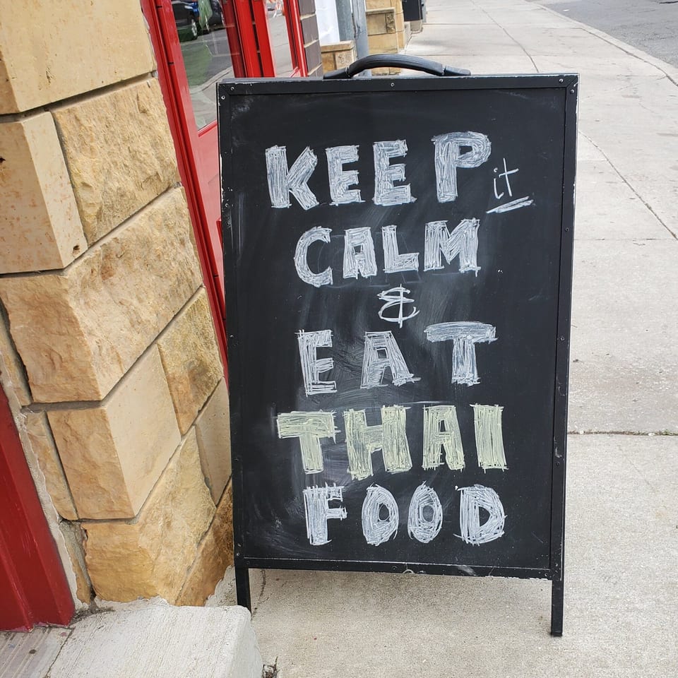 Chalkboard sign outside Baan Thai restaurant reads: "KEEP it CALM & EAT THAI FOOD".